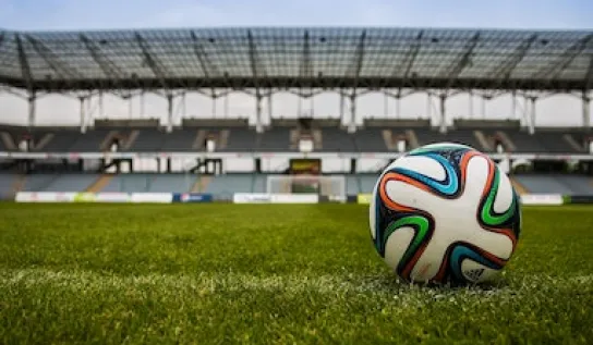 A soccer ball on a field with a stadium in the background.