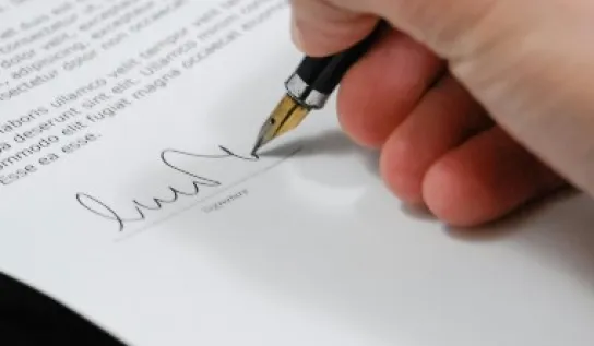 Someone signing their signature on a piece of paper with a pen