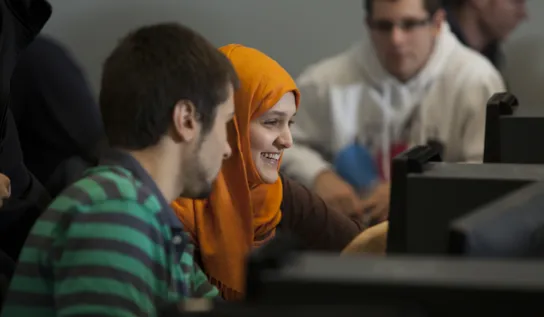 two students smiling while using a computer