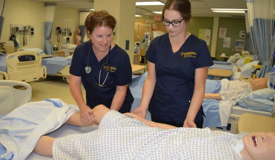 Nursing students working with a dummy in a clinical lab.