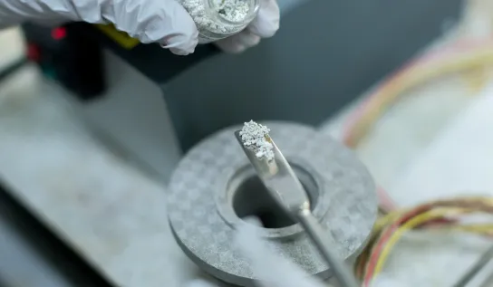 Gloved hands measuring out silver coloured substance
