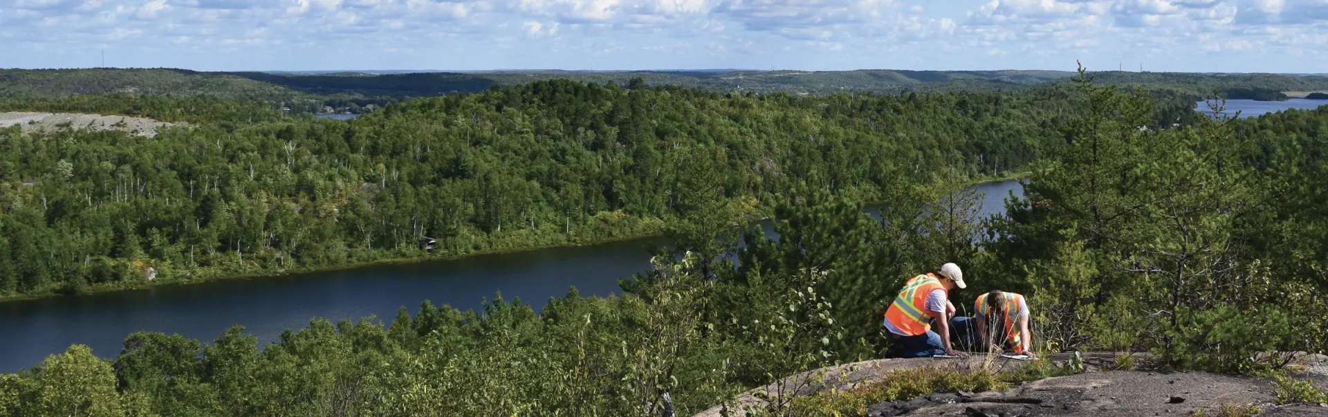 Two Laurentian Geology students working on a rocky mountain overlooking a lake.