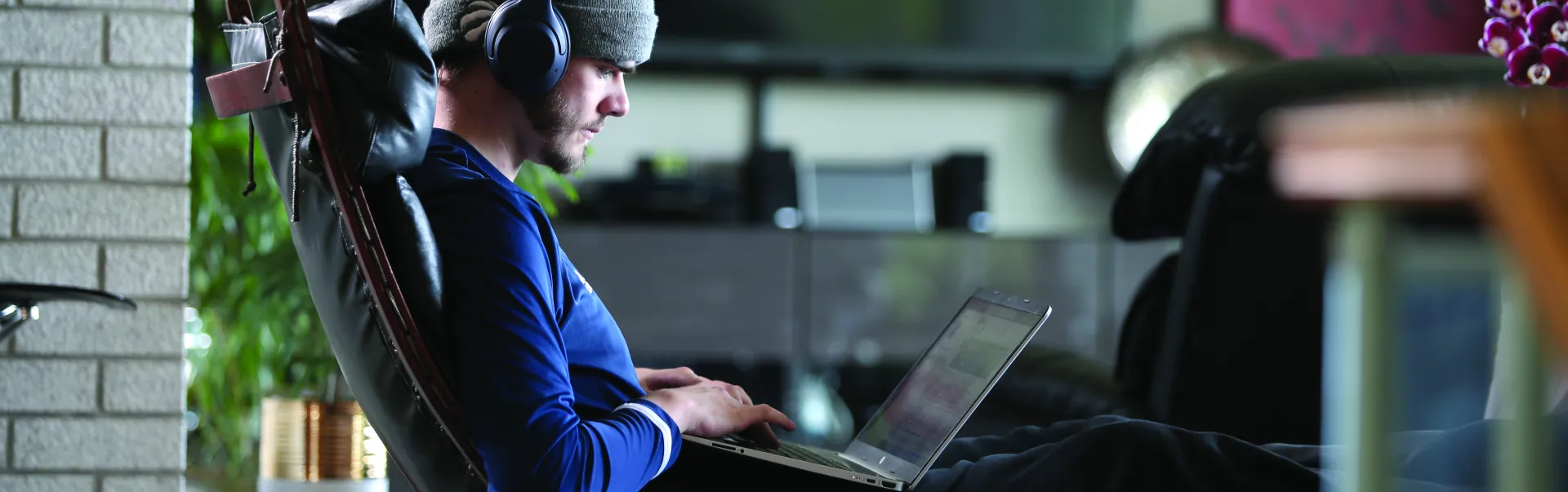 A student wearing headphones studies on a laptop while seated in a lounge area on campus.
