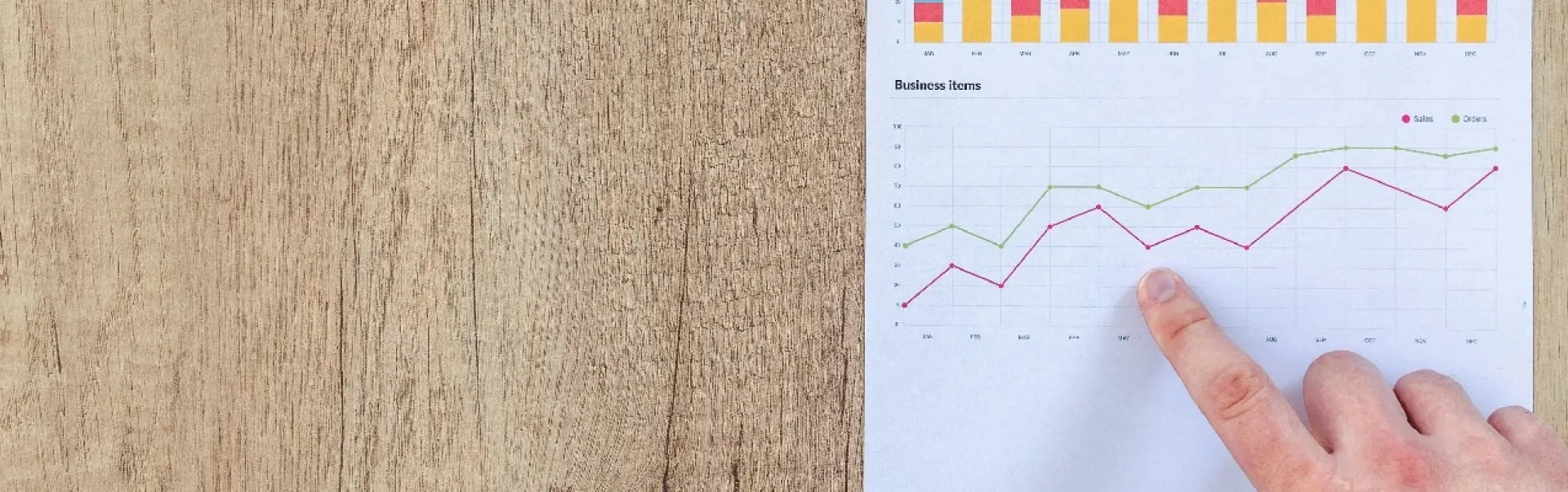 A hand holding a pen and a piece of paper with graphs on it.