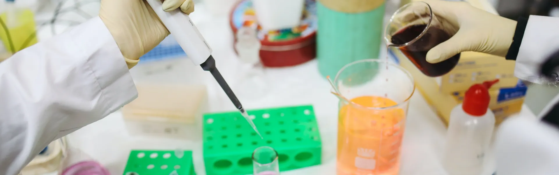 A student pipetting into a test tube while another student is pouring a red liquid into a beacon