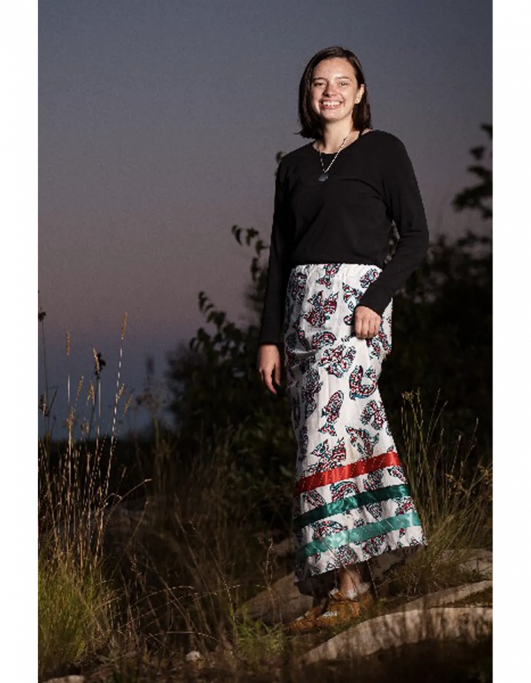 Renée standing outside in the tall grass at sunset.