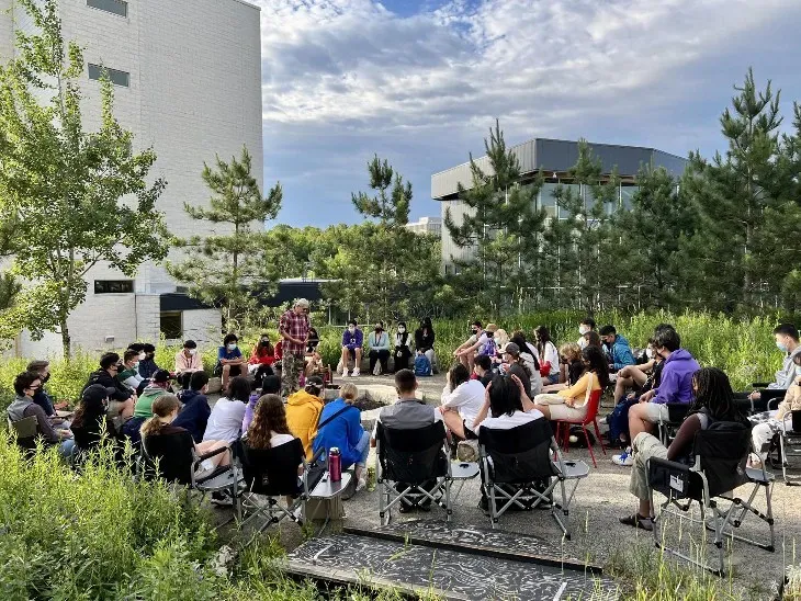 A group of people sitting in lawn chairs by a fire pit.