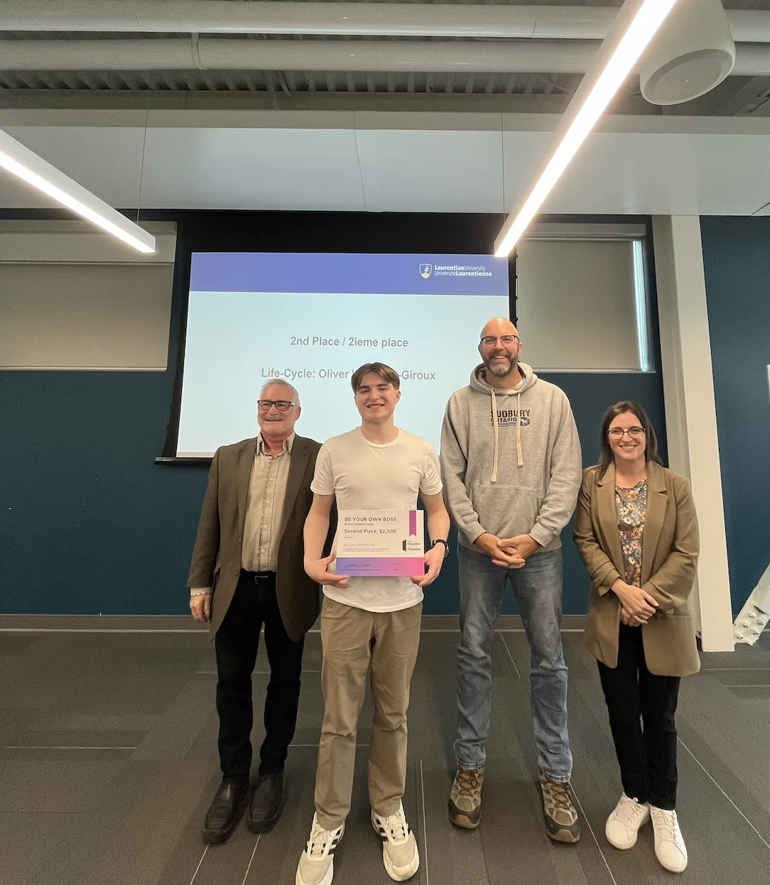 Second-place BYOB winner Oliver Wuthrich-Giroux stands in the center of the stage holding his certificate.
