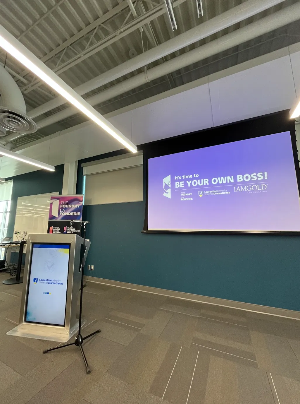 The presentation stage at Laurentian University's Jim Fielding Innovation Space, featuring a screen that reads 'It’s time to BE YOUR OWN BOSS!' with The Foundry and IAMGOLD logos.
