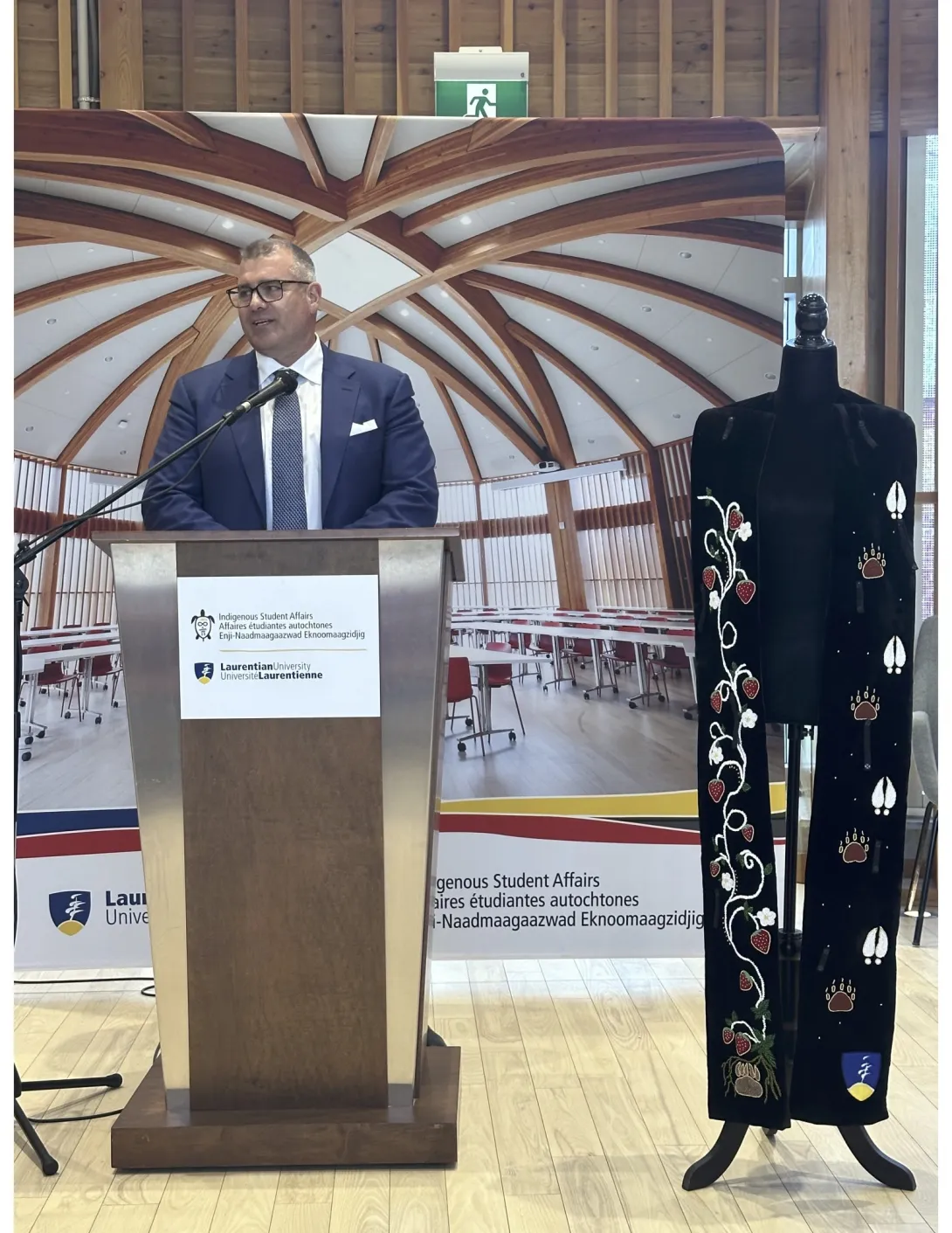 Chancellor Kristan Straub speaks at Laurentian University during the presentation of the custom Ajijaak Doodem Chancellor’s Medallion, displayed beside him.