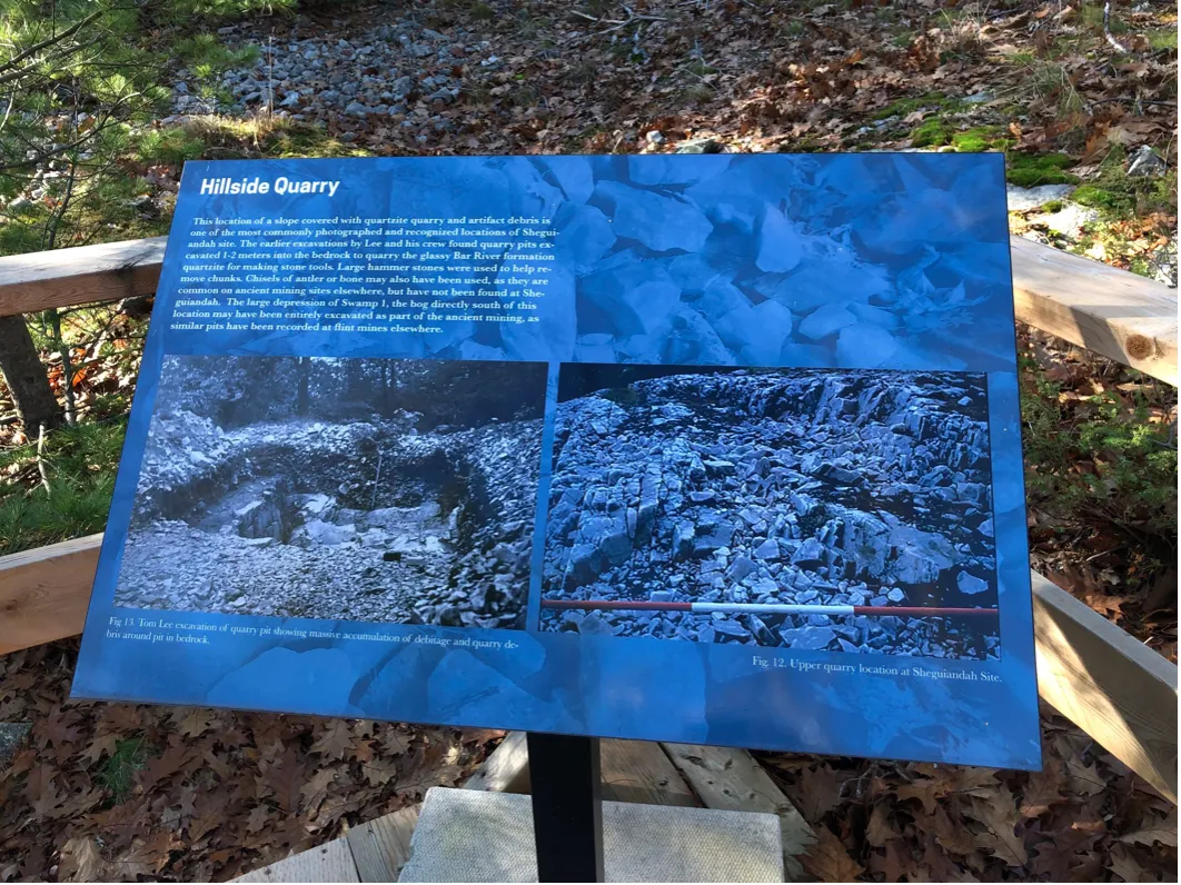 A close-up view of an educational sign at the Sheguiandah Archaeological Site titled "Hillside Quarry." The panel features white text detailing the site's geological history and two historical black-and-white photographs showing early archaeological quarry excavations and rock formations.