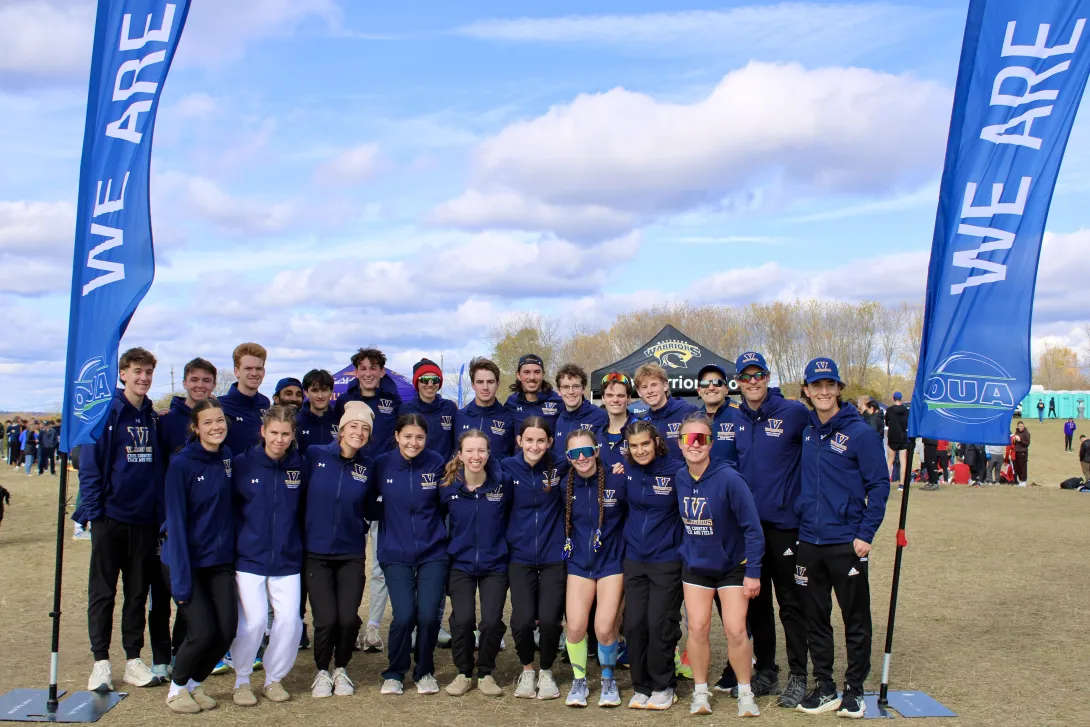 The Laurentian Voyageurs cross-country team poses together for a group photo framed by blue OUA banners at a meet.
