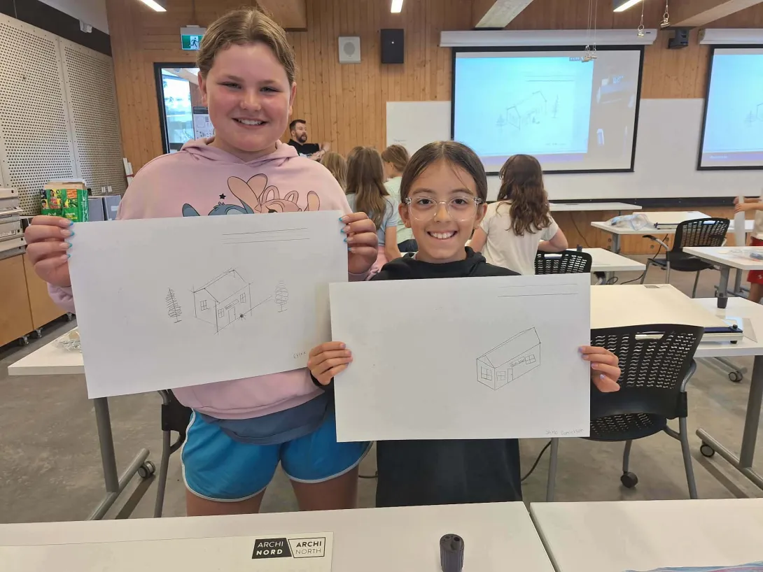 Two young campers smile broadly as they hold up their completed architectural perspective sketches during a studio session at the McEwen School of Architecture.