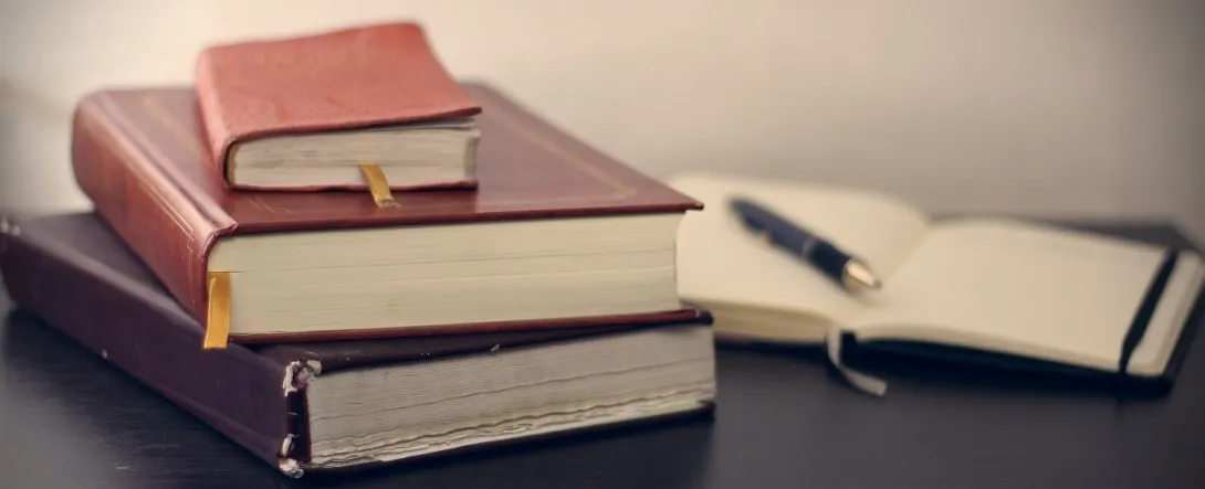 A pile of books and an open notebook on a desk.