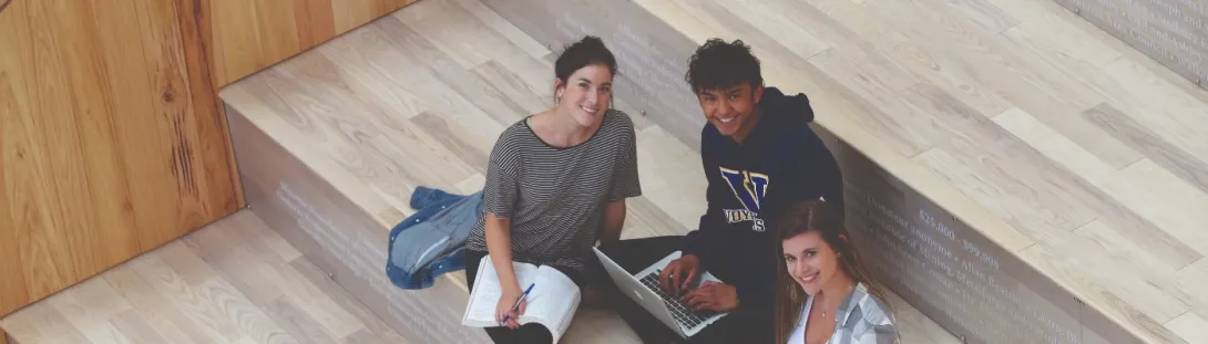Three students sitting on the steps in the atrium while studying